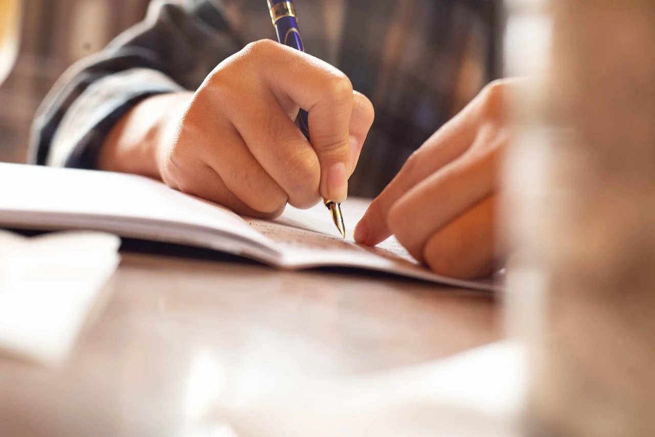 Pessoa escrevendo em um caderno com uma caneta, destacado foco na escrita e na mão segurando a caneta, ideal para conteúdo de estudos, poesias ou anotações.